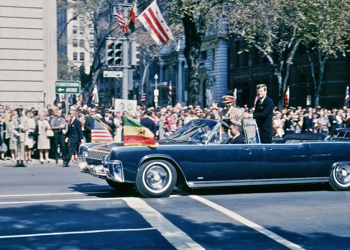An open car flying Ethiopian and American flags passes crowds beside a Pennsylvania Avenue street sign